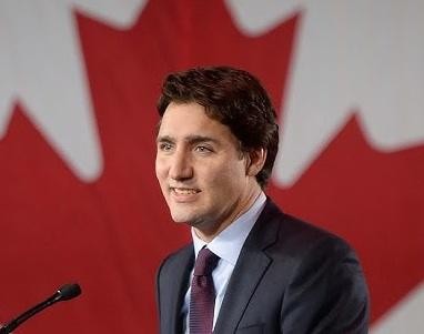 Justin Trudeau przemawiający z podium, w garniturze, z flagą Kanady w tle, wyrażający zaangażowanie i determinację.