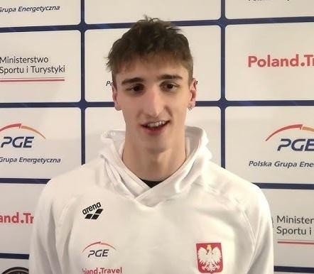 Ksawery Masiuk podczas treningu, wykonujący styl grzbietowy, z widocznymi kroplami wody i skupionym wyrazem twarzy, podkreślający jego determinację.