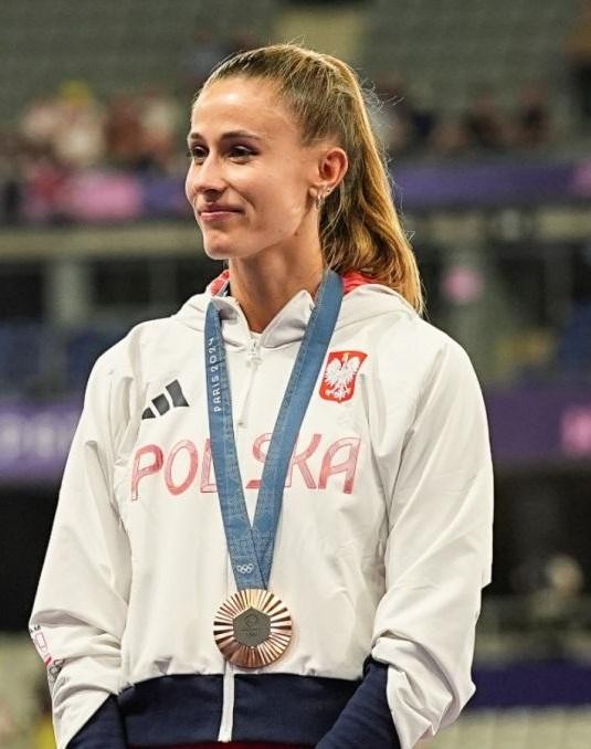 Natalia Bukowiecka uśmiechnięta w stroju sportowym, w swobodnej pozie, z widocznym logo Adidas.