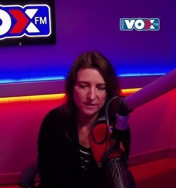 Renata Dąbkowska podczas występu na żywo, śpiewająca do mikrofonu, z widocznym światłem scenicznym i elementami zespołu w tle.