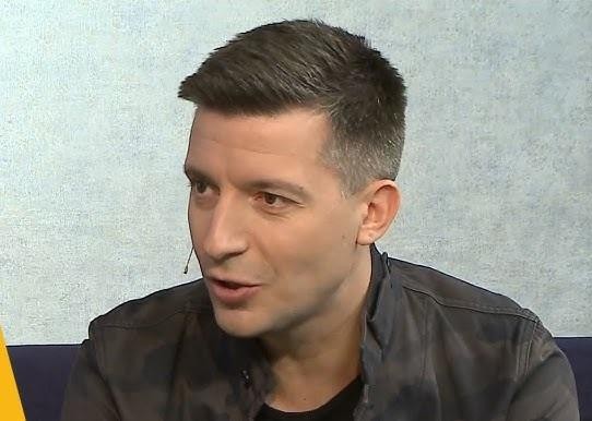 Michał Cessanis w ujęciu zbliżonym, zamyślony, w tle subtelnie zamazane książki lub instrumenty muzyczne, nawiązujące do jego wykształcenia muzykoterapeutycznego.