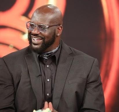 Shaquille O'Neal w stroju akademickim, z dumą trzymający dyplom, symbolizujący jego osiągnięcia edukacyjne.
