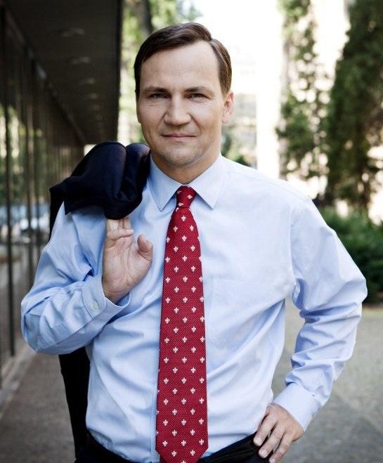 Radosław Sikorski przemawiający energicznie z mównicy, z dynamicznym gestem dłoni, w tle widoczna sala konferencyjna.