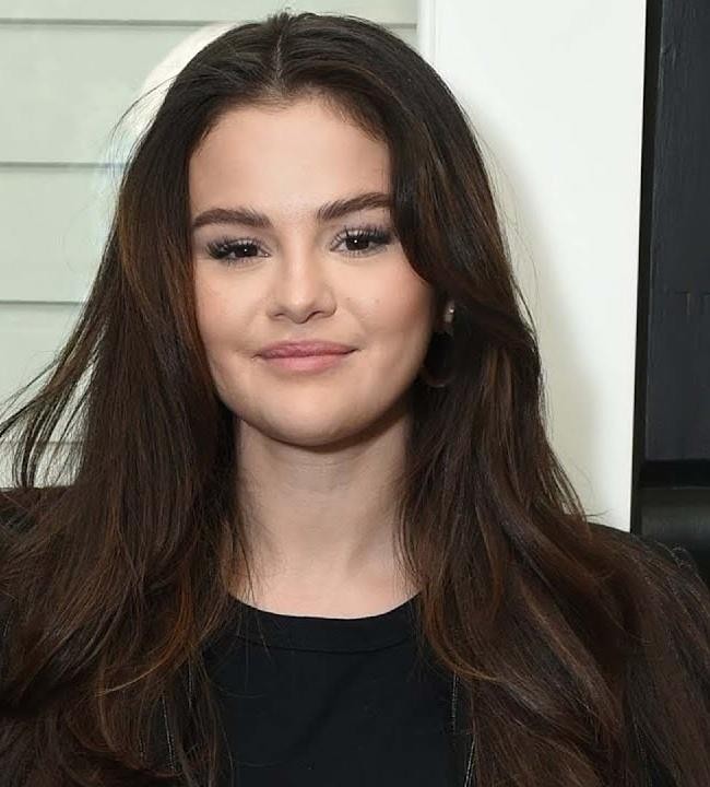 Selena Gomez używająca telefonu, z rozmytym tłem sugerującym aktywność w mediach społecznościowych.