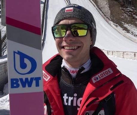 Jakub Wolny lądujący na ośnieżonej skoczni, z zaciętą miną i rozpryskującym się śniegiem.